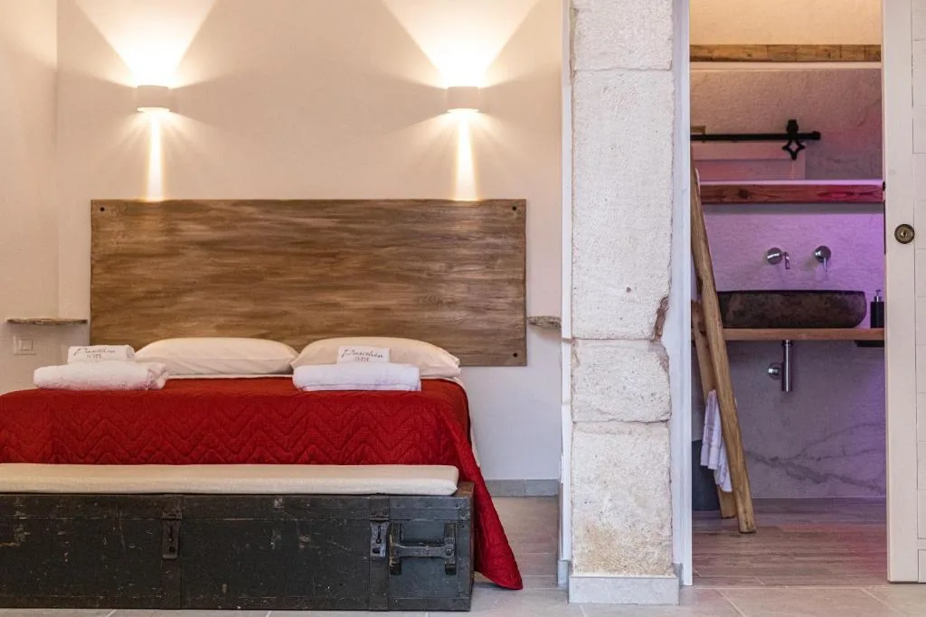 Bed beneath a wooden headboard with warm wall lights and an old stone column